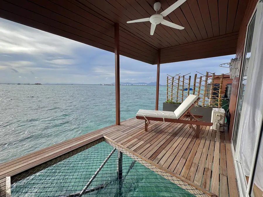Private balcony with glass viewing floor and suspended overwater hammock net at Sand Bay Resort